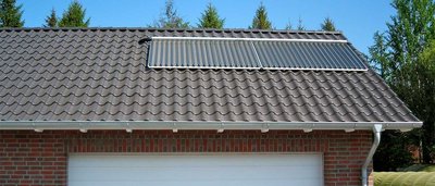 Auf dem Dach sind glänzende Solarpanels installiert, die sich harmonisch in die wellenförmigen Ziegel einfügen, umgeben von Natur.