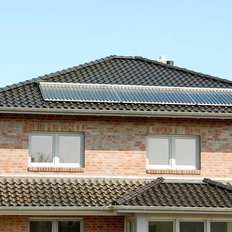 Die Fassade eines Ziegelhauses zeigt große Fenster und ein Dach mit glänzenden Solarpanelen, ideal für nachhaltige Energie.