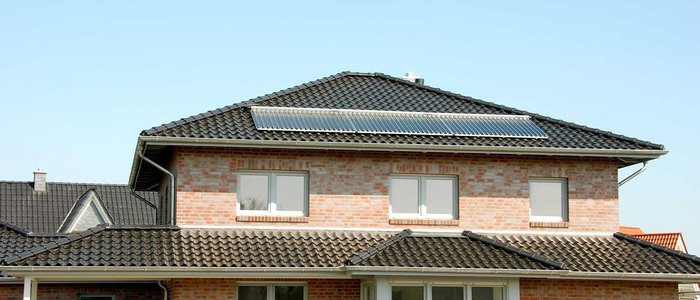 Die Fassade eines Ziegelhauses zeigt große Fenster und ein Dach mit glänzenden Solarpanelen, ideal für nachhaltige Energie.