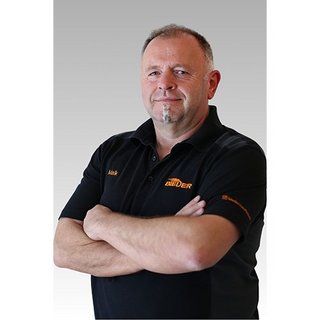 In einem schwarzen Polohemd mit BIEDER-Logo präsentiert sich ein lächelnder Mann, der seine Arme vor der Brust verschränkt.