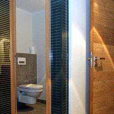 Ein moderner Sanitärbereich mit zwei getrennten Toiletten, die durch elegante Holztüren und Glaswände abgetrennt sind.