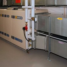 Ein Raum mit verschiedenen Lüftungsanlagen, darunter große Metallkanäle und eine weiße Maschine an der Wand.