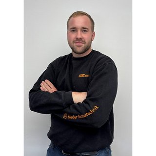 Der Mann lächelt leicht, während er in einem schwarzen Sweatshirt mit dem Logo einer Firma posiert, die auf Haustechnik spezialisiert ist.