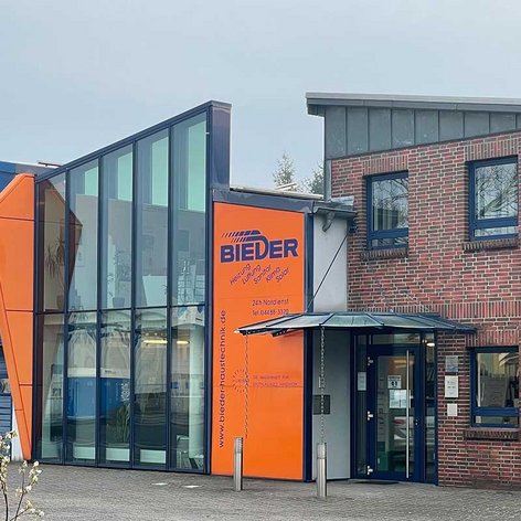 Das Firmengebäude von BIEDER zeigt eine innovative Architektur mit großen Fenstern und einem markanten orangefarbenen Akzent.