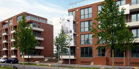 Ein Werbebanner an einem der Gebäude kündigt neue Wohnungen an, während Autos am Straßenrand parken.