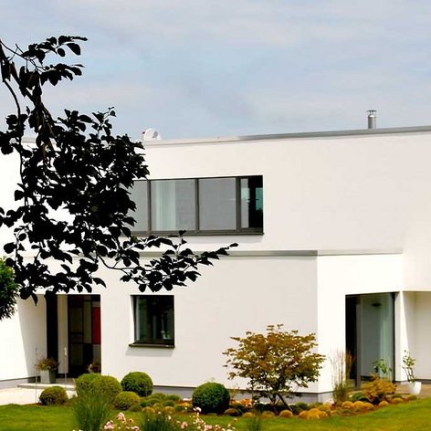 Ein elegantes, minimalistisches Haus mit einem hellen Äußeren, das in einer ruhigen Umgebung am Wasser steht.