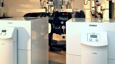 In einem technischen Raum sind zwei Vaillant-Heizsysteme sichtbar, die mit verschiedenen Rohren und Messgeräten verbunden sind.